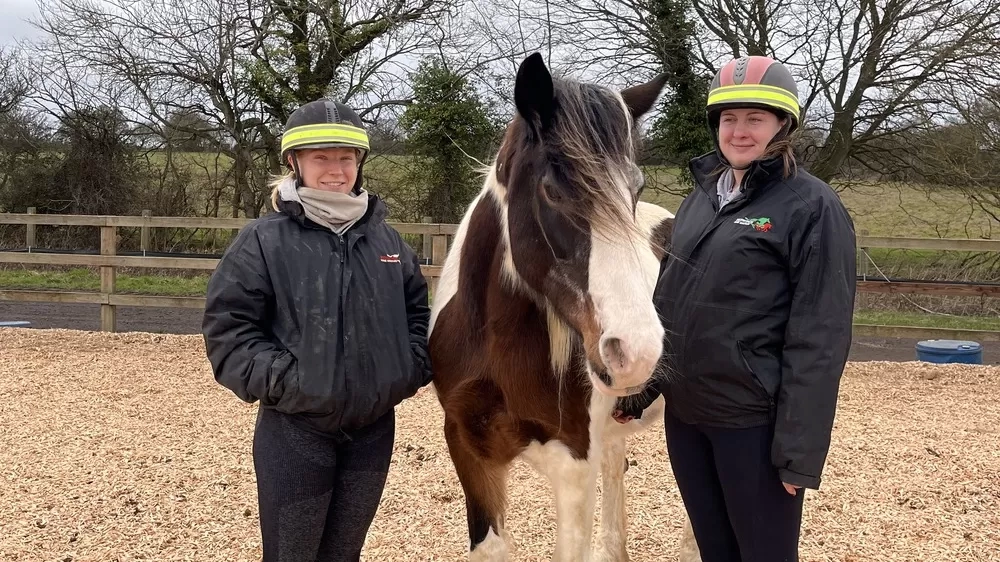 Two members of staff standing with a brown and white pony
