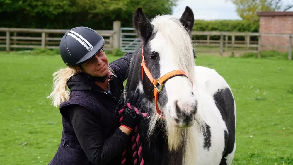 A Redwings equine carer cuddles a black and white pony in her grass paddock.