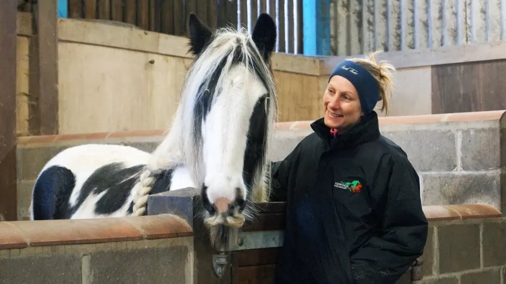 Redwings Equine Behaviour Manager Sarah Hallsworth stands in the stables of the Behaviour Centre smiling at a black and white pony.