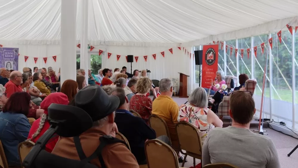 A seated crowd in a white marquee listen to author Suzie Fletcher at the Redwings Book Festival.