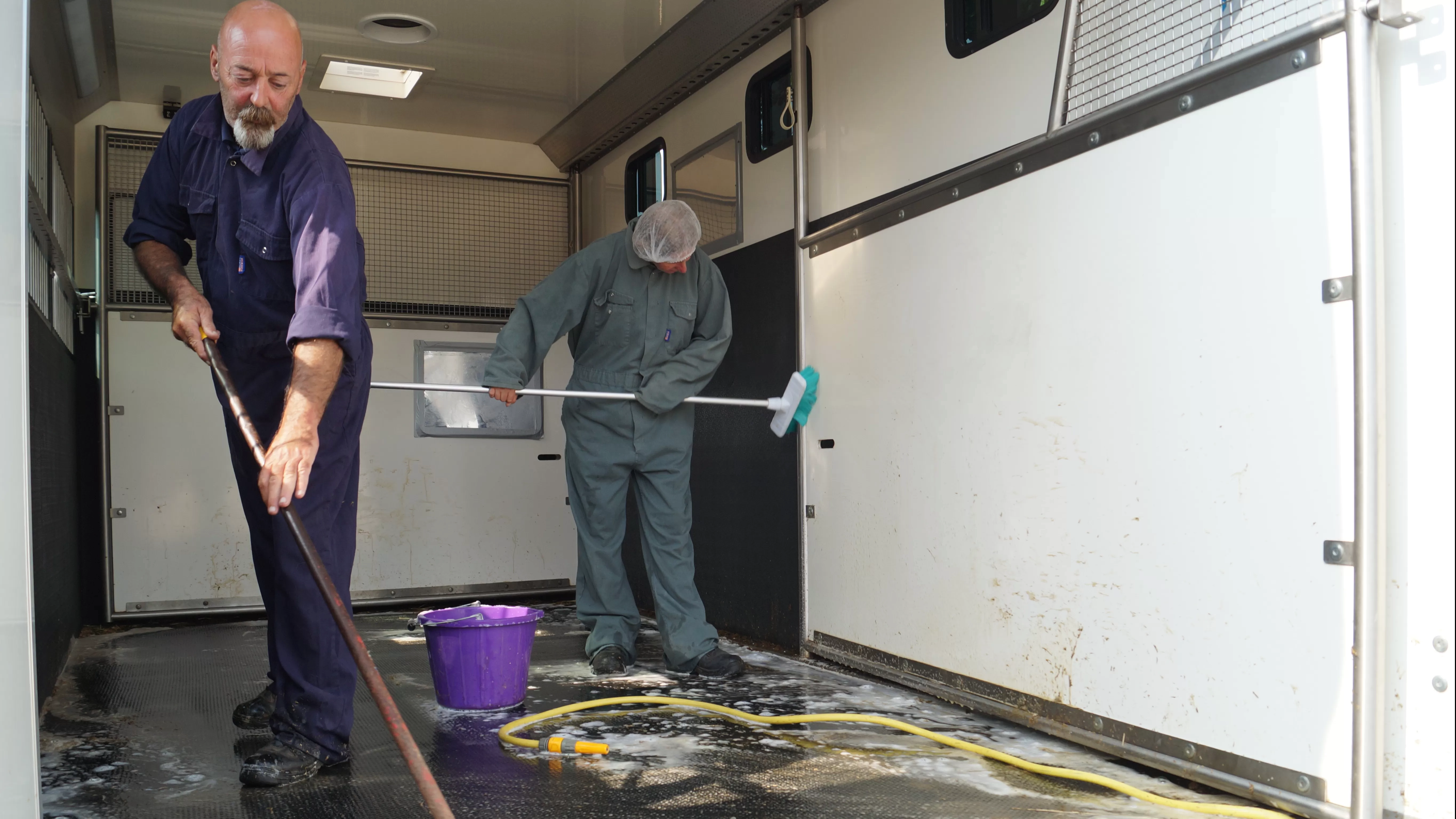 Photo of two people in overalls scrubbing a horsebox