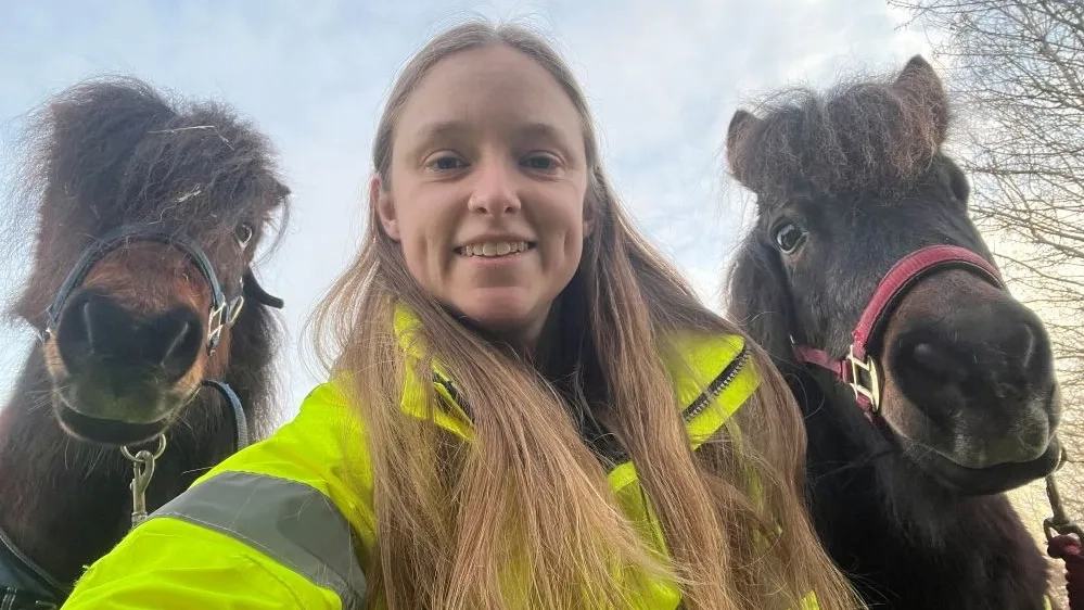 Photo of ponies Dennis and Merry on either side of their carer Kristi