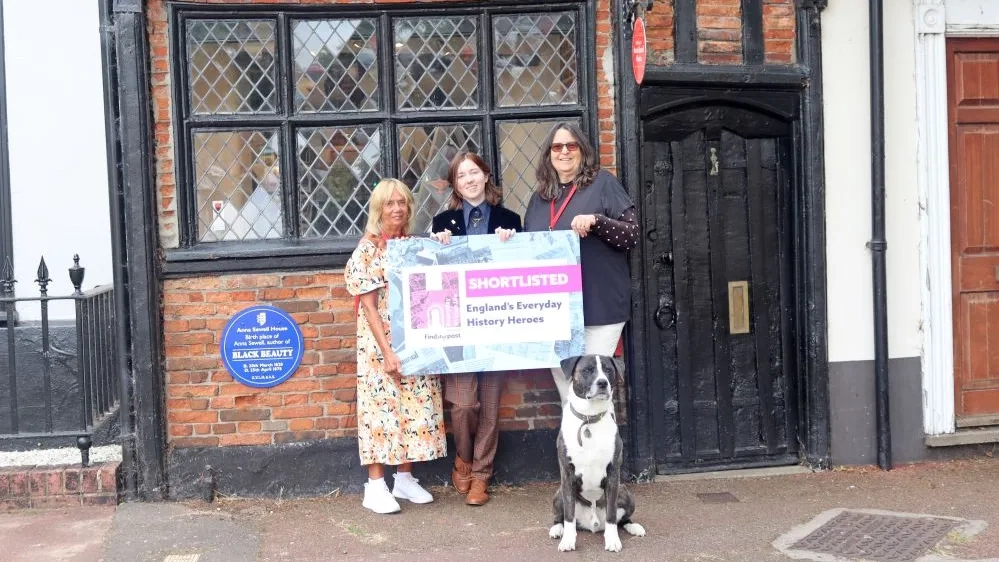 People and a dog outside Anna Sewell House holding a 'Shortlisted England's Everyday Hereos'