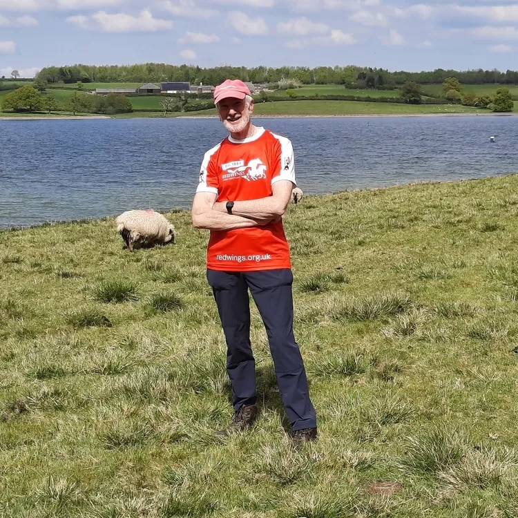 Trustee Ian, wearing a Redwings branded sports shirt, stood in front of a lake and some sheep