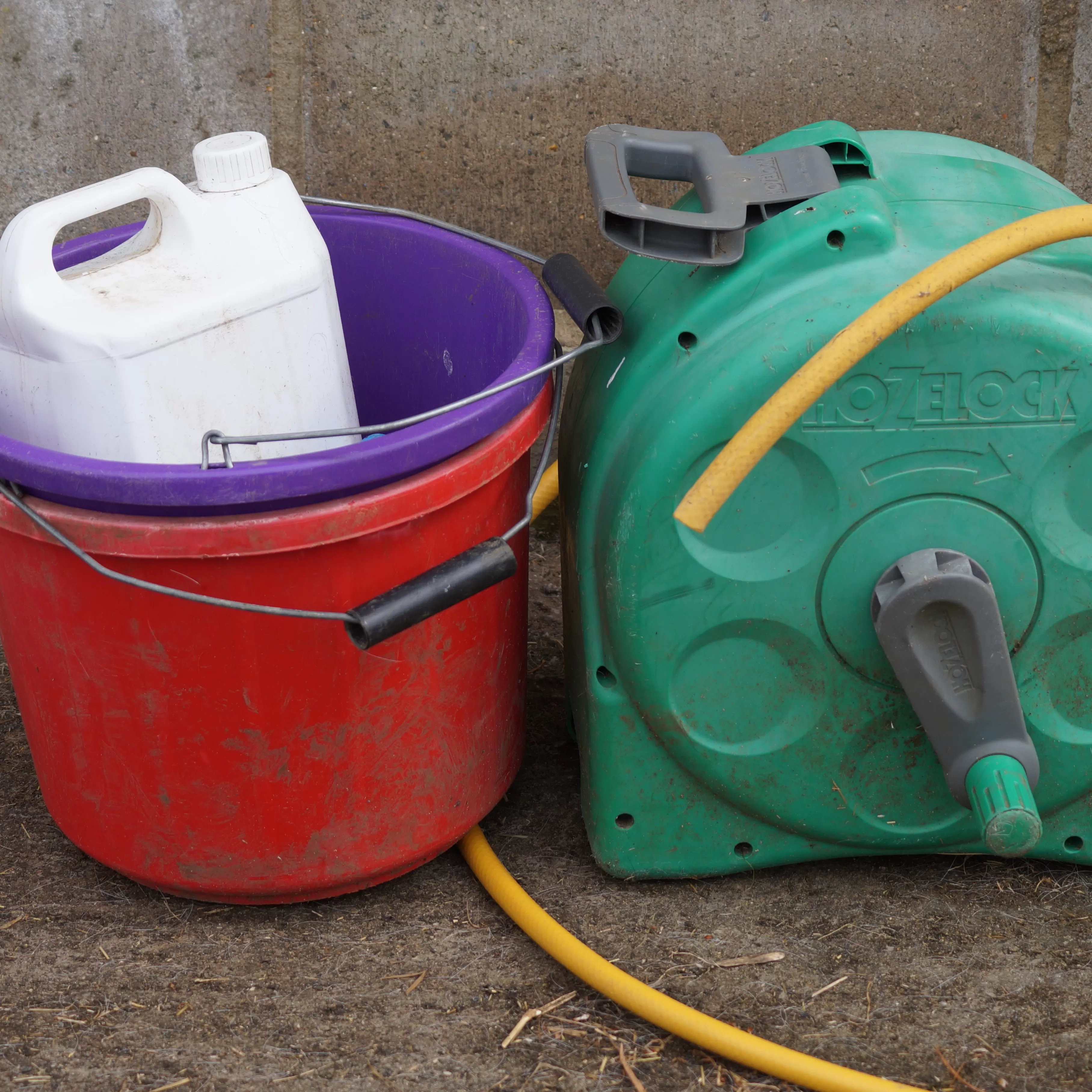 A container of disinfectant sitting inside a bucket, next to a hosepipe storage reel