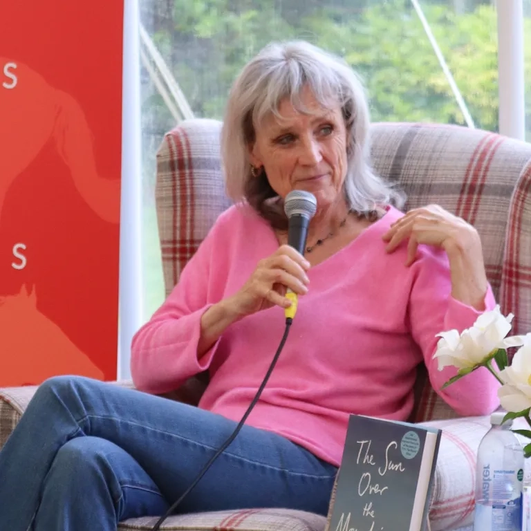 Photo of Suzie sat in a chair speaking into a microphone at the Redwings Book Festival. 