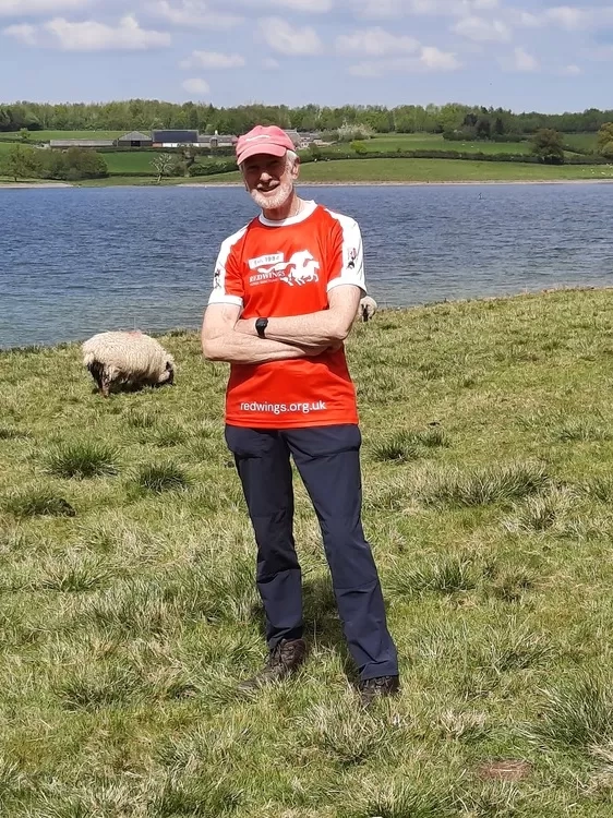 Trustee Ian, wearing a Redwings branded sports shirt, stood in front of a lake and some sheep