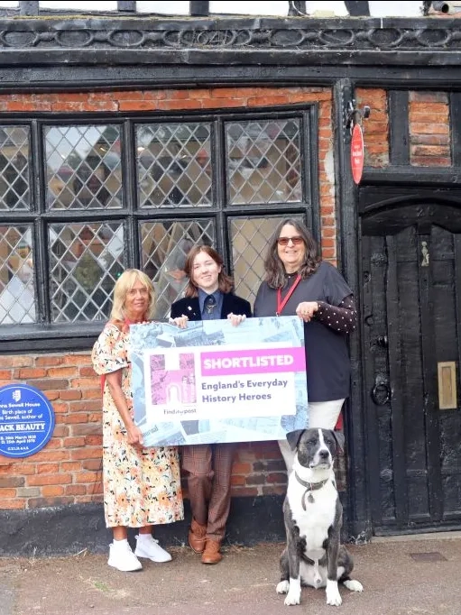 People and a dog outside Anna Sewell House holding a 'Shortlisted England's Everyday Hereos'